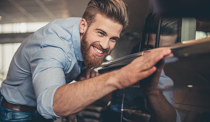 Hombre mirando admirado su auto nuevo comprado con un préstamo para autos