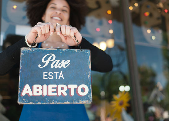 Persona promocionando un desarrollo económico que sostiene un cartel que dice "we're open" (abierto) con las manos.